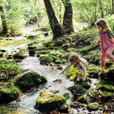 Two children having an adventure, climbing and stepping in a river exploring a beautiful natural area. Beautiful, idyllic and tranquil childhood moment. Sisters or friends, innocent and free Family Creek Exploration